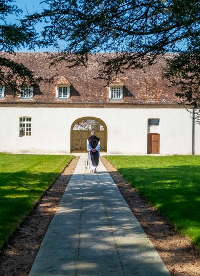 Un moine marche mains dans le dos dans une allée devant l'abbaye de Sept-Fons.